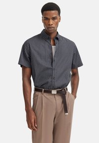 Kurzarmhemd in Marineblau mit einem geometrischen Muster, kombiniert mit hellbraunen Hosen und einem braunen Gürtel mit einer silbernen Schnalle.