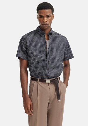 Kurzarmhemd in Marineblau mit einem geometrischen Muster, kombiniert mit hellbraunen Hosen und einem braunen Gürtel mit einer silbernen Schnalle.