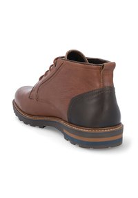 Botín de cuero marrón hasta el tobillo con un acabado suave, tacón oscuro en contraste y acentos texturizados. Cuenta con una suela de goma con rayas multicolores.