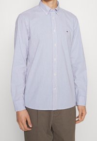 Chemise à manches longues, blanche avec des rayures bleues, en tissu coton, col boutonné, avec un petit logo sur la poitrine.