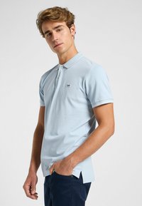 Ljusa blå polo t-shirt i bomull med korta ärmar, en krage och en liten "Lee"-logotyp på vänster bröst. Har sidsplitter längst ner.