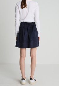 Marineblauwe suède rok met een elastische tailleband en een uitlopende design, gecombineerd met een wit shirt met lange mouwen en casual sneakers.