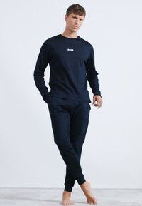 Camisa negra de manga larga con el logo "BOSS" y pantalones a juego. Material de algodón, corte relajado, textura suave y sin patrones visibles.