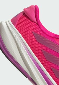 Chaussure de sport rose avec une tige en mesh texturé, des accents violets et une semelle intermédiaire blanche dégradée vers le violet. Design incurvé pour le confort.