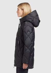 Veste matelassée noire avec capuche, dotée d'une fermeture éclair à l'avant, de poches latérales et d'un écusson logo sur la manche. Texture lisse.