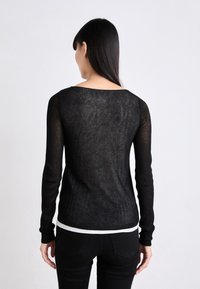 Haut noir à manches longues avec une texture transparente, un col large et un ourlet blanc en bas. S'ajuste parfaitement, mettant en valeur les détails de la silhouette.