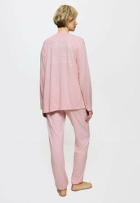 Rosa Schlafanzug-Set mit langen Ärmeln und Hose, aus weichem Stoff. Der Rücken hat weißen Text und ein lässiges Design.