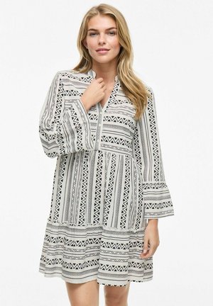 Robe à manches longues avec un motif géométrique noir et blanc, décolleté en V, manches évasées et jupe à volants. Fabriquée en tissu léger.