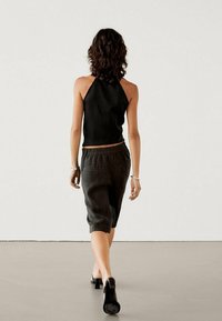 Schwarzes Neckholder-Top kombiniert mit einem dunklen Leinenrock, der einen elastischen Bund hat. Getragen mit schwarzen High Heels, von hinten gezeigt.