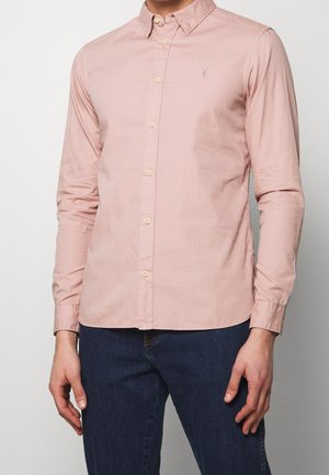 Camisa de botones de color rosa claro con cuello y mangas largas; presenta un pequeño emblema en el pecho y cierres de botón estándar.