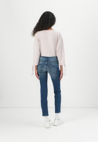 Lys rosa, stripete langermet topp med løs passform og sidebånd, kombinert med tettsittende blå jeans med baklommer og smale ankler. Hvite joggesko.