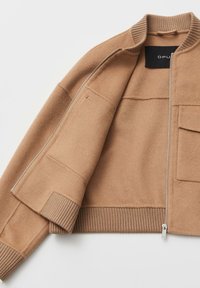 Giacca bomber color cammello con collo e polsini a coste, chiusura a cerniera e tasca laterale. Realizzata in tessuto morbido e caldo con una texture liscia.