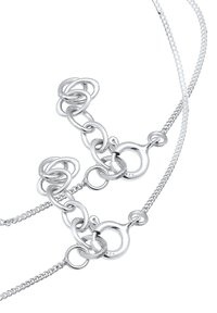 Sølvsmykke bestående av sammenkoblede løkkedesign i varierende størrelse og form. Jevn tekstur med en polert finish.