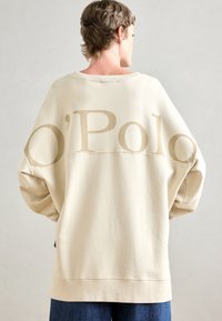 Crème oversized sweatshirt met een ronde halslijn, voorzien van lichtbruine "O'Polo" tekst op de rug en smalle boorden. Soepele textuur, casual pasvorm.