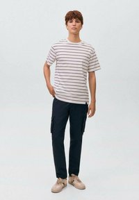 Prugasta majica kratkih rukava u krem i mornarsko plavoj boji, uparena s mornarsko plavim cargo hlačama koje imaju više džepova i bež tenisicama.