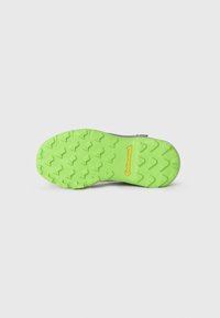 Suela de zapato con un patrón de tracción pronunciado, que presenta un material de goma de color verde brillante y un logotipo en relieve en amarillo. Superficie plana y agarre texturizado.
