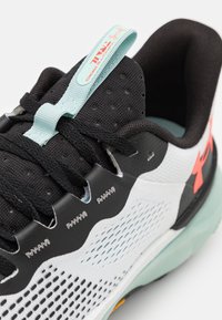 Close-up of a white and black sports shoe with black laces, a teal pull tab labeled “Infinite Pro,” and an orange logo on the side.