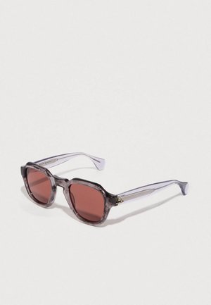 Óculos de sol com tonalidade roxa e uma armação robusta e transparente. As lentes são de um vermelho escuro. Apresenta hastes curvas e um discreto detalhe em dourado.