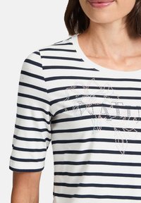 Striped short-sleeve top in white and navy, featuring a round neckline and a decorative design made of rhinestones on the front.