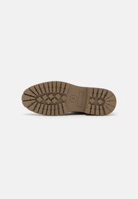 Sole in gomma marrone con scanalature profonde e superficie texturizzata. Presenta un marchio e un logo rotondo vicino al tallone.