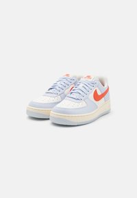 Baskets Nike Air Force 1 avec un dessus en cuir bleu clair et blanc, un swoosh rouge et une semelle en caoutchouc crème avec un motif texturé.