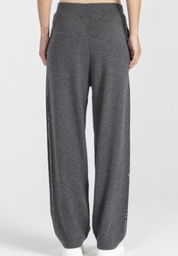 Szare, szerokie spodnie dresowe wykonane z miękkiego materiału, z regulowanym sznurkiem w pasie, bocznymi kieszeniami oraz ozdobnymi guzikami wzdłuż zewnętrznych szwów.