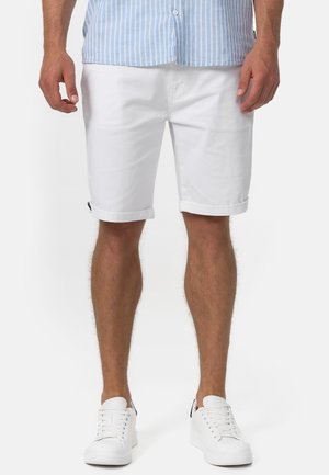 Weiße Baumwollshorts mit aufgerollten Säumen, im Slim-Fit-Schnitt. Getragen mit weißen Sneakern und kombiniert mit einem hellblau gestreiften Hemd.