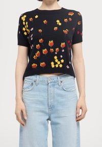 Suéter negro de punto de manga corta con bordado floral colorido en amarillo, rojo y blanco sobre una superficie texturizada. Combina con jeans de color azul claro.