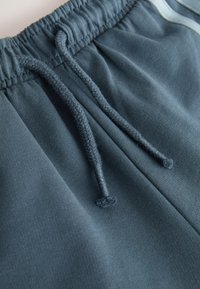 Close-up of dark gray sweatpants waistband with elastic band and two loose braided drawstrings against a plain background.