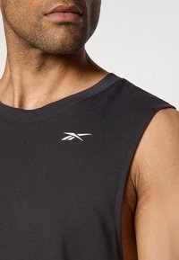 Débardeur de sport noir sans manches en tissu lisse, avec un petit logo blanc sur la poitrine gauche et un col rond.