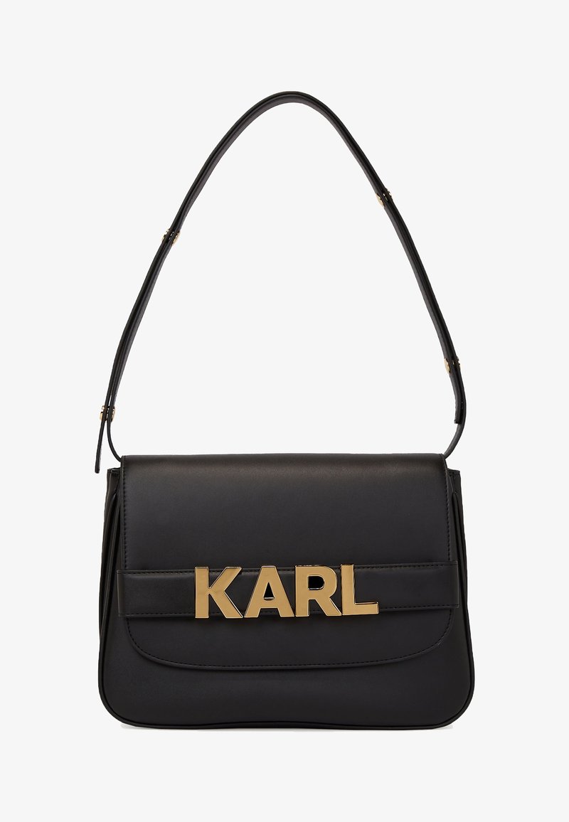 Sac à épaule en cuir noir avec un rabat rectangulaire et des lettres métalliques dorées formant "KARL" sur la sangle avant.