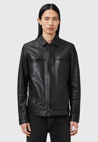 Veste en cuir noire avec un col, fermeture éclair à l'avant, poches poitrine et manches longues ; texture lisse et design ajusté.