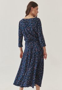 Robe marine à motif floral en rose et bleu. Présente des manches trois-quarts et une jupe fluide qui tombe sous le genou.