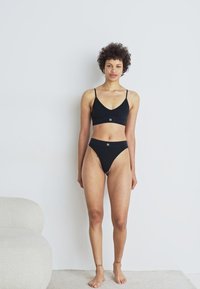 Zwart ondergoedset met een driehoekige bralette met dunne bandjes en een hoge slip. Glad materiaal met minimale details en logo-accenten.