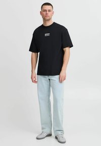 Zwarte katoenen t-shirt met korte mouwen en een grafische tekstprint op de borst, gecombineerd met lichtblauwe jeans en grijze sneakers.