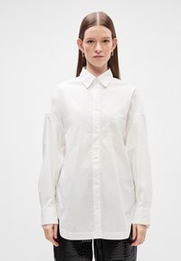 Λευκό πουκάμισο με μακριά �μανίκια, κλασικό γιακά, κουμπιά μπροστά και μία τσέπη στη στήθη. Λείο ύφασμα, oversized εφαρμογή και χαλαρά μανίκια.