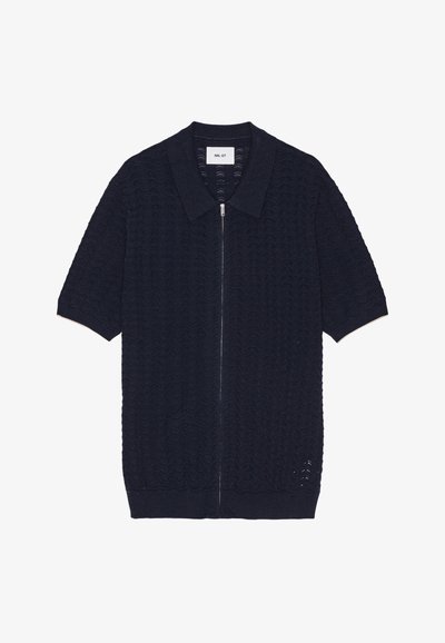 Laivastonsininen neule lyhythihainen pusero, jossa on vetoketju ja rakenteellinen aaltoilu, sekä klassinen kaulus ja Ribbaushelma.