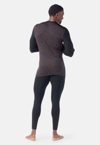 Camicia a maniche lunghe con motivo geometrico in tonalità di marrone e blu; maniche nere e leggings neri aderenti. Tessuto morbido e elastico.