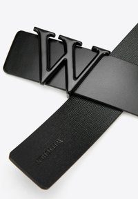 Cinturón negro con un destacado logo "W" negro brillante, con una correa texturizada y un detalle en el extremo liso y plano.