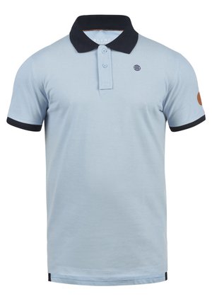 Lyseblå polo-skjorte med svart krage, matchende ermekanter og et globe-logo på brystet. Har to knapper ved halslinjen.