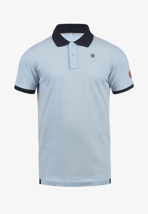 Lyseblå polo-skjorte med svart krage, matchende ermekanter og et globe-logo på brystet. Har to knapper ved halslinjen.