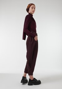 Bordeaux lange mouw top met een gedrapeerde halslijn, gecombineerd met losse donkerbordeaux broek. Zwarte platform schoenen met dikke zolen.
