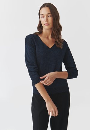 Marineblauer Strickpullover mit V-Ausschnitt, gerippten Bündchen und schimmernder Textur. Kombiniert mit schwarzen Hosen, hat er eine taillierte Passform.