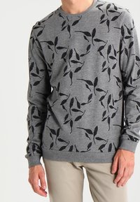 Sweat-shirt gris avec motifs de feuilles noirs, col rond, manches longues et poignets côtelés. Tissu texturé, coupe décontractée.