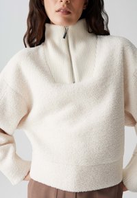 Cremfarbener Fleece-Pullover mit hohem geripptem Kragen, halbem Reißverschluss und verkürztem Design. Die Oberfläche hat ein strukturiertes, weiches Gefühl.