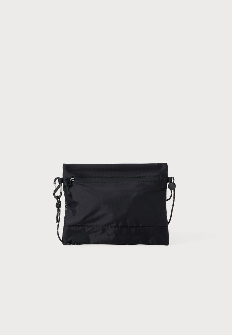 Bolso de hombro negro de nailon con cremallera en la parte superior, correa ajustable y detalles de costura mínimos. Textura suave y diseño sin adornos.