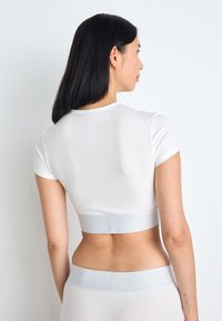Haut court blanc à manches courtes, avec une texture lisse et une bande élastique grise claire à la taille, associé à un bas assorti.