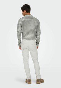 Chemise à carreaux grise et verte, associée à un pantalon blanc. La chemise possède un col et des manches longues, avec un détail de l'empiècement au dos.