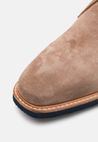 Scarpa in camoscio marrone chiaro con punta arrotondata. Presenta una suola in pelle cucita color tan e una suola esterna in gomma blu scuro. Texture morbida.