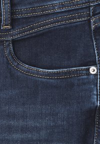 Tmavě modré džíny z denimu s přední kapsou, viditelným švem a stříbrným knoflíkem. Materiál vypadá hladce a odolně.